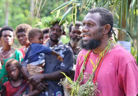 Ein Mann spricht zur Gruppe. Er trägt ein pinkes Shirt und Pflanzenschmuck.